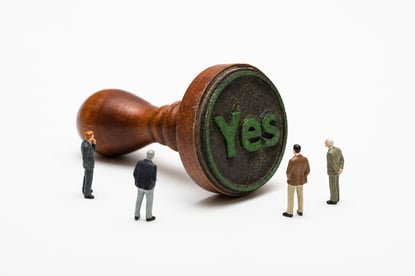 Miniature People Observing Green Yes Stamp on White Background